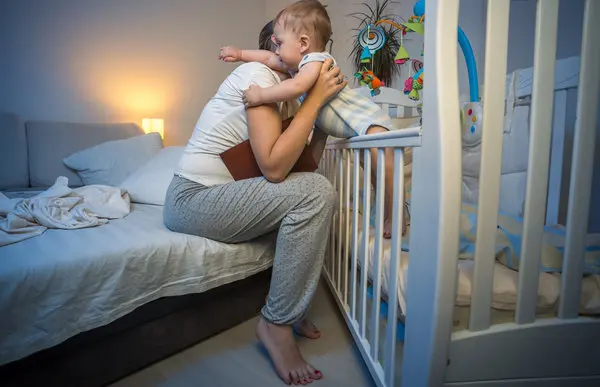 پدری که به آرامی پاهای نوزاد خود را قبل از خواب برای رفع کولیک ماساژ میدهد.